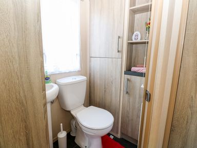 A small bathroom with a toilet sink cabinet built into the wall and shelves with towels at Freddys Lodge Foxburrow Hang in Fritton