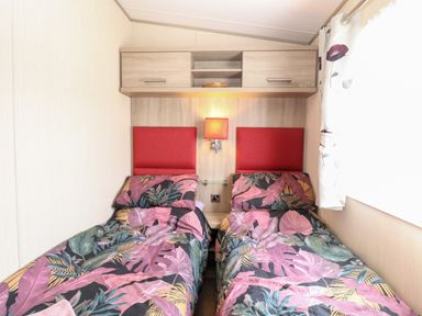 A bedroom with two single beds with patterned bedding and red headboards at Freddy's Lodge Foxburrow Hang in Fritton