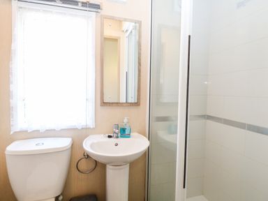 A bathroom with a toilet, pedestal sink with soap dispenser, mirror, and a glass shower enclosure at Freddys Lodge Foxburrow Hang in Fritton