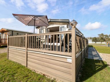 A deck with outdoor seating and umbrella attached to a mobile home at Freddys Lodge Foxburrow Hang in Fritton
