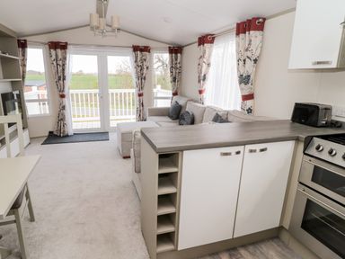 A living area with a sofa, curtains, a dining table, and a kitchen counter with an oven and toaster at Moonlight Lodge in Bockenfield Country Holiday Park near West Thirston