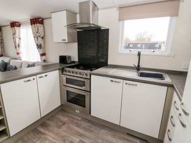 A kitchen with white cabinets a stove a sink and a window at Moonlight Lodge in Bockenfield Country Holiday Park near West Thirston