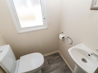 A small bathroom with a white toilet a white sink a toilet paper holder and a frosted window at Moonlight Lodge in Bockenfield Country Holiday Park near West Thirston
