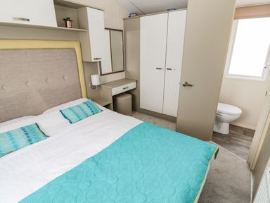 A bedroom with a bed a wardrobe a dressing table and an en suite bathroom at Moonlight Lodge in Bockenfield Country Holiday Park near West Thirston