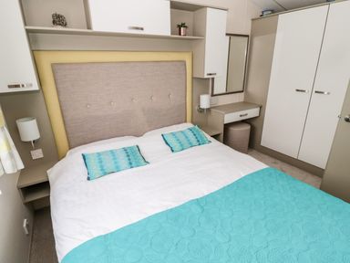 A bedroom with a double bed with blue cushions and bedspread a dressing table with mirror and wardrobe at Moonlight Lodge in Bockenfield Country Holiday Park near West Thirston