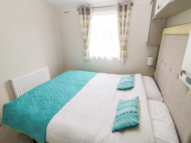 A bedroom with a double bed blue pillows and a blue quilt by a window with curtains at Moonlight Lodge in Bockenfield Country Holiday Park near West Thirston
