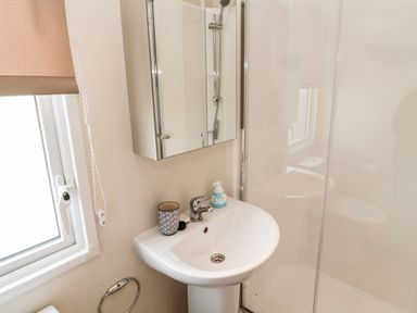 A bathroom with a sink and mirror next to a shower enclosure and a window at Moonlight Lodge in Bockenfield Country Holiday Park near West Thirston
