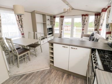 An open plan kitchen dining and living area with dining table chairs sofa and television at Moonlight Lodge in Bockenfield Country Holiday Park near West Thirston