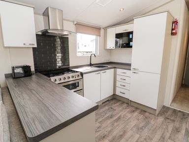 A kitchen with white cabinets a stainless steel stove a black toaster and a window at Moonlight Lodge in Bockenfield Country Holiday Park near West Thirston