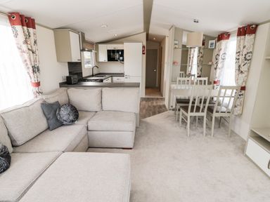 A living room with a beige sofa and pillows next to a kitchen with white cabinets and a dining table with chairs at Moonlight Lodge in Bockenfield Country Holiday Park near West Thirston
