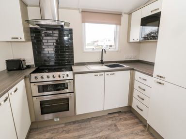 A kitchen with stainless steel oven microwave toaster white cabinets and window at Moonlight Lodge in Bockenfield Country Holiday Park near West Thirston