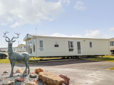 A mobile home with windows and a door parked on a paved area with a deer statue and rocks in front at Moonlight Lodge in Bockenfield Country Holiday Park near West Thirston