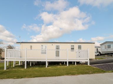 A white caravan with a raised deck and railing outside on grass at Moonlight Lodge in Bockenfield Country Holiday Park near West Thirston