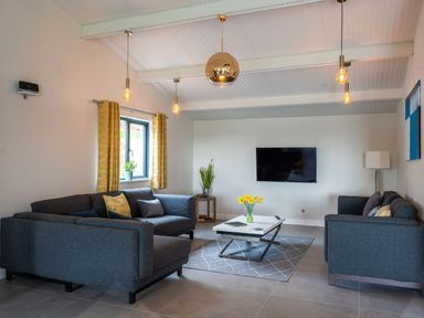 A living room with two gray sofas a coffee table with flowers a wall-mounted tv and hanging pendant lights at Quantock Barn in Stockland near Honiton