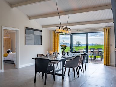 A dining room with a table set for six and sliding glass doors opening to a patio at Quantock Barn in Stockland near Honiton