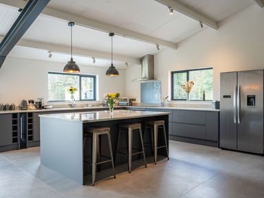 A kitchen with an island and bar stools with flowers on the countertop at Quantock Barn in Stockland near Honiton