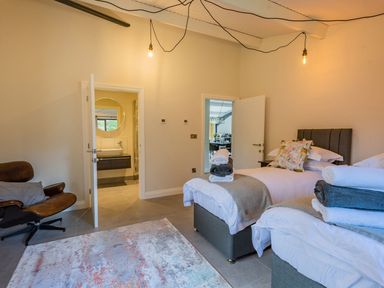A bedroom with two single beds a leather chair a rug and two open doors showing a bathroom and another room at Quantock Barn in Stockland near Honiton