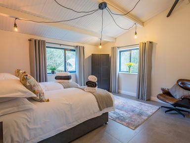 A bedroom with two beds towels on beds a wardrobe and a leather chair at Quantock Barn in Stockland near Honiton