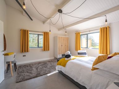 A bedroom with a bed and yellow curtains and a wooden wardrobe and a grey rug at Quantock Barn Stockland near Honiton