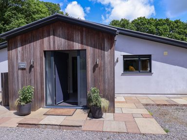 The exterior entrance of a building with wooden paneling gravel and paving stones at Quantock Barn in Stockland near Honiton
