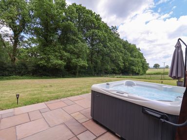 An outdoor hot tub on a tiled patio overlooking a grassy field and trees at Quantock Barn in Stockland near Honiton