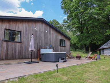 A patio with a hot tub umbrella chairs and a fire pit outside a wooden building at Quantock Barn in Stockland near Honiton