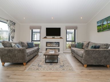 A living room with two grey sofas a wooden coffee table and a wall-mounted television at Meadow Lodge in Lifton