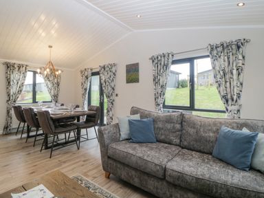 A living room with a gray sofa and a dining area with a table and six chairs at Meadow Lodge in Lifton