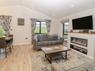 A living room with a gray sofa blue pillows wooden coffee table patterned rug wall mounted television and fireplace at Meadow Lodge in Lifton