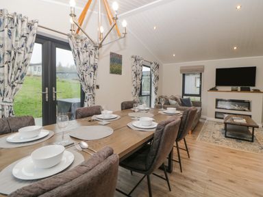 A dining table set with plates bowls and glasses next to a living area with sofas a coffee table a mounted TV and a fireplace at Meadow Lodge in Lifton