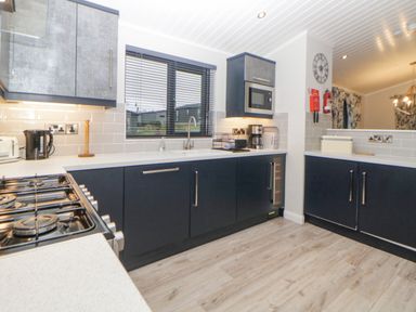 A kitchen with black lower cabinets gray upper cabinets a gas stove a microwave coffee maker and window blinds at Meadow Lodge in Lifton