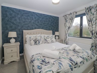 A bedroom with a bed bedside tables lamps and a window with curtains at Meadow Lodge in Lifton