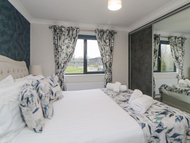 A bedroom with a bed and patterned cushions near windows with matching curtains and a mirrored wardrobe at Meadow Lodge in Lifton