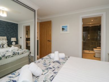 A bedroom with a bed featuring floral bedding rolled towels on the bed a bedside table with a lamp a wooden door a mirrored wardrobe an open door leading to a bathroom at Meadow Lodge in Lifton