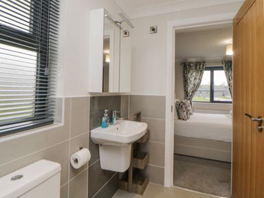 A bathroom with a sink toilet and window next to a bedroom with a bed and curtains at Meadow Lodge in Lifton