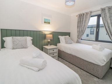 A bedroom with two single beds a bedside table with lamp and a window with curtains at Meadow Lodge in Lifton