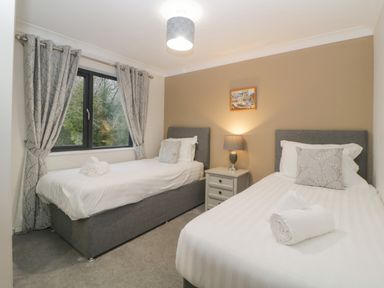 A bedroom with two single beds a nightstand lamp and window with curtains at Meadow Lodge in Lifton