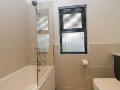 A bathroom with a bathtub shower and a window with blinds at Meadow Lodge in Lifton