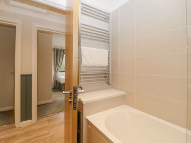 A bathroom with a bathtub towel rail and an open door showing a bedroom at Meadow Lodge in Lifton