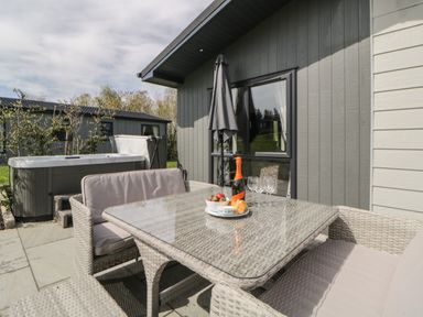 An outdoor patio with wicker furniture a glass table an umbrella a hot tub and food and drinks on the table at Meadow Lodge in Lifton
