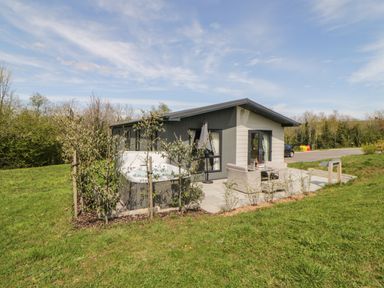 A small house with a patio table and chairs and a hot tub on a grassy lawn at Meadow Lodge in Lifton
