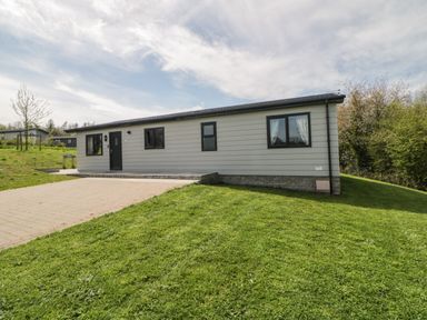 A single-story house with horizontal siding and black-framed windows on a lawn with a paved driveway at Meadow Lodge in Lifton