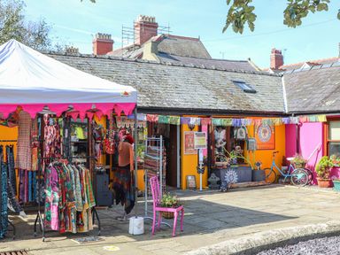 An outdoor market stall with colorful clothes and a pink chair outside a building with orange and pink walls at Cobblers Cottage in Beaumaris
