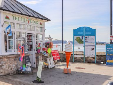 An ice cream kiosk with outdoor display racks and signs near a waterfront at Cobblers Cottage in Beaumaris