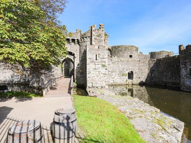 A stone castle with a wooden bridge over a moat and two wooden barrels near a tree at Cobblers Cottage in Beaumaris