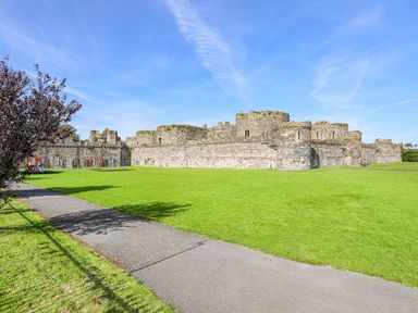 A stone castle with a playground and green lawn in front with a sidewalk at Cobblers Cottage in Beaumaris