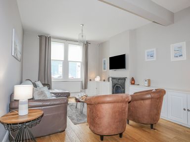 A living room with leather chairs a sofa a wall-mounted TV and windows at Cobblers Cottage in Beaumaris