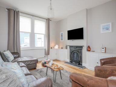 A living room with leather sofas a wooden coffee table a wall-mounted TV and a fireplace at Cobblers Cottage in Beaumaris