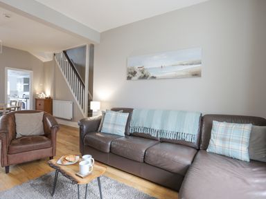A living room with a brown leather sofa and armchair a wooden table with cups and croissants and a painting on the wall at Cobblers Cottage in Beaumaris