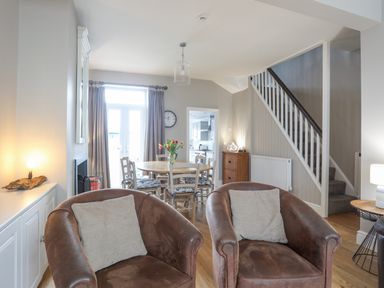 A living room with two brown chairs a dining table with chairs and a staircase at Cobblers Cottage in Beaumaris